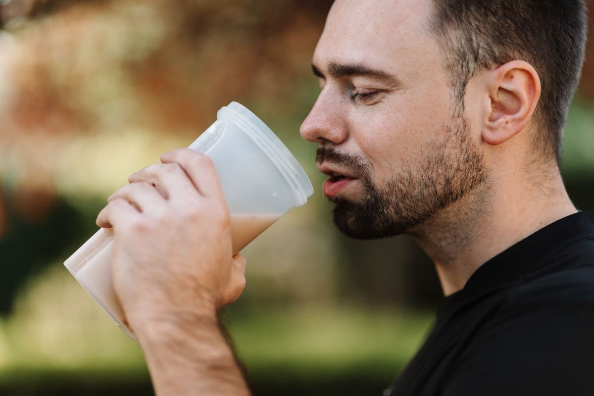 Skäggig man som dricker en smoothie ur ett glas utomhus