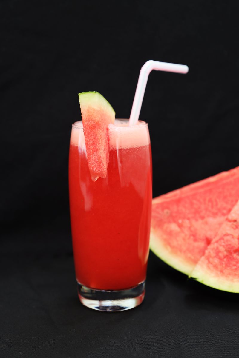 Glas vattenmelonjuice med sugrör bredvid en skiva vattenmelon